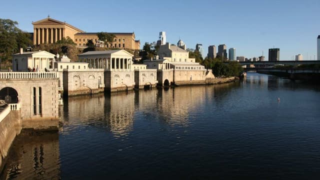 A cluster of Greek Revival buildings along a riverfront, with larger buildings in the background.
