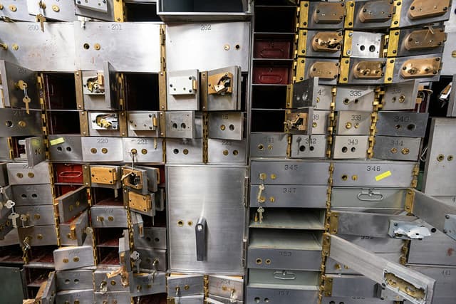 A photo of a wall of safe deposit boxes, most of which are open and empty. 