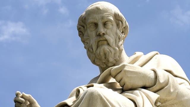 A statue of a man, with wavy hair and beard, and a serious expression.